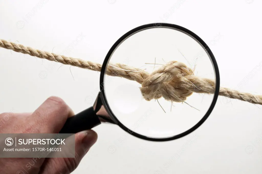 A hand holding a magnifying glass magnifying a knot in a rope