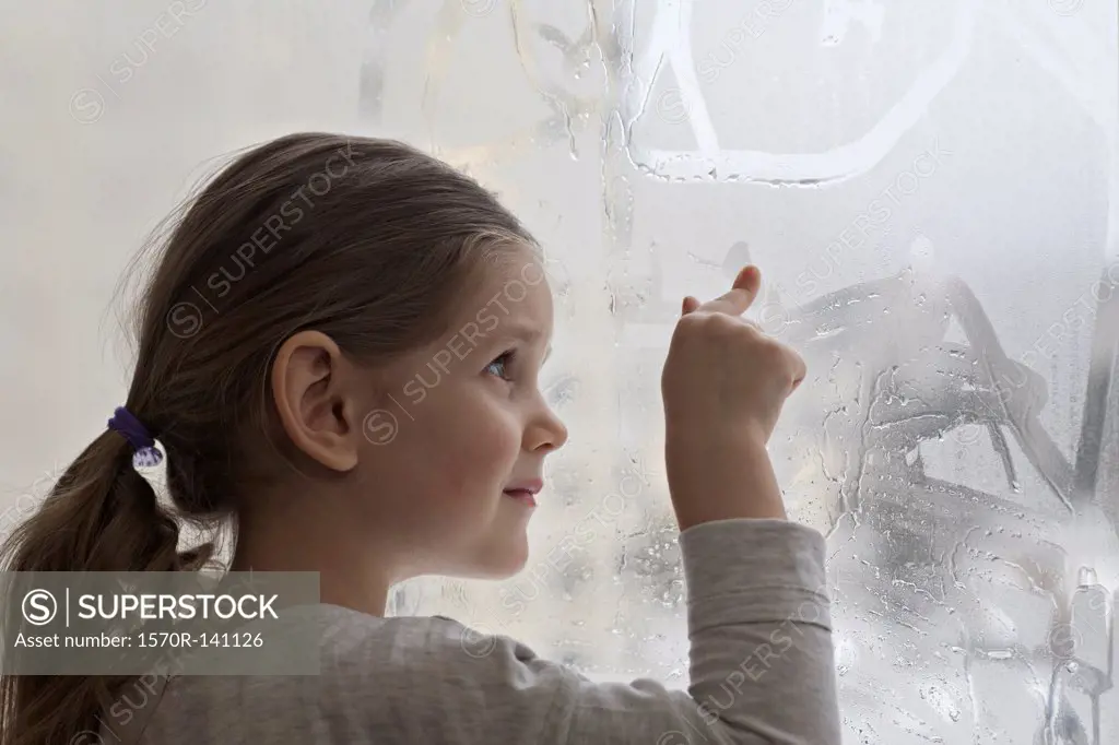 A girl drawing in condensation on glass