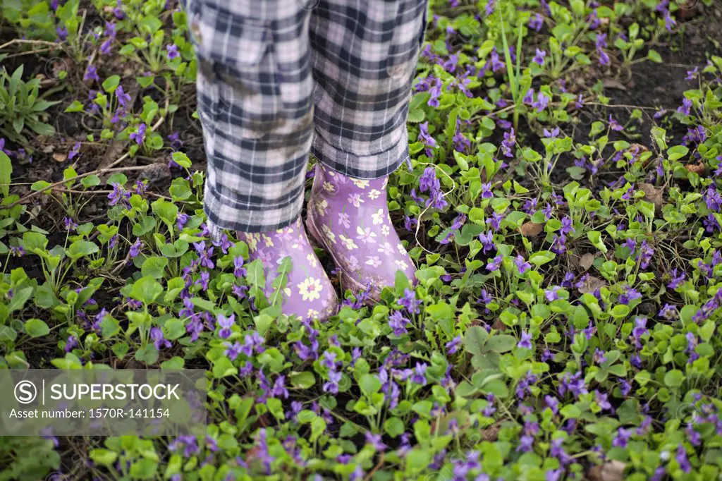 Low section of a girl standing in a garden with gumboots