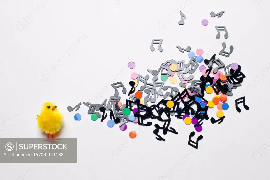 A toy Easter chick next to a group of musical notes and confetti