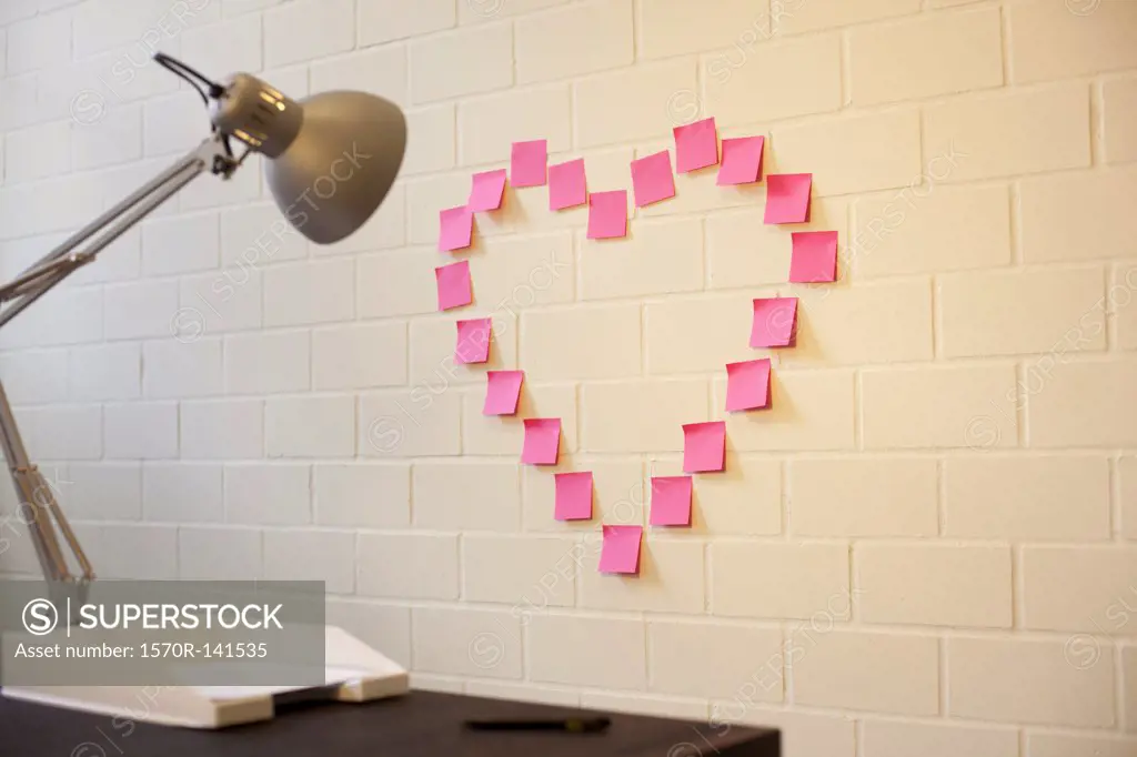 Adhesive notes arranged into the shape of a heart on a wall next to a desk