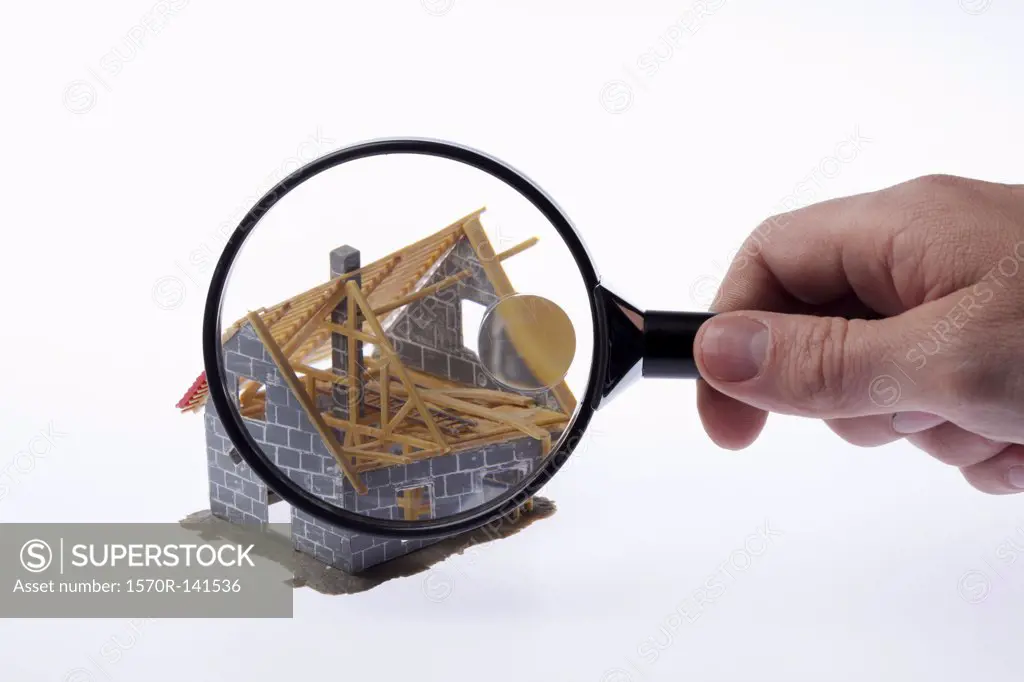 A human hand holding a magnifying glass up to a partially constructed miniature house model