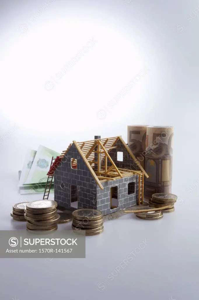 A partially constructed house with European Union currency and coins around it