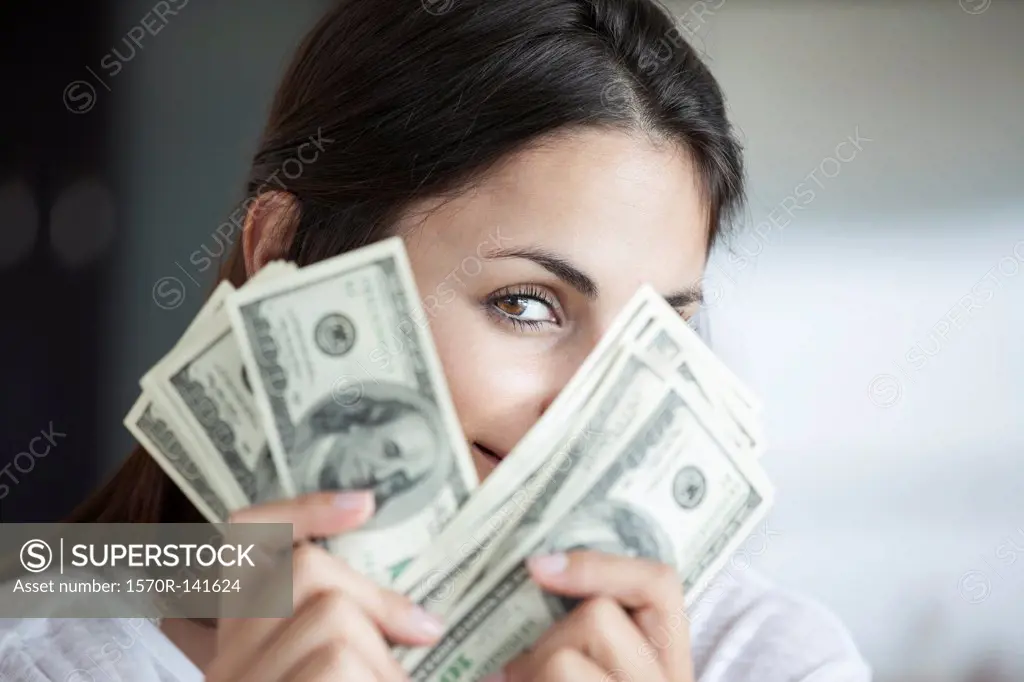 Woman peeking behind hundred dollar bills