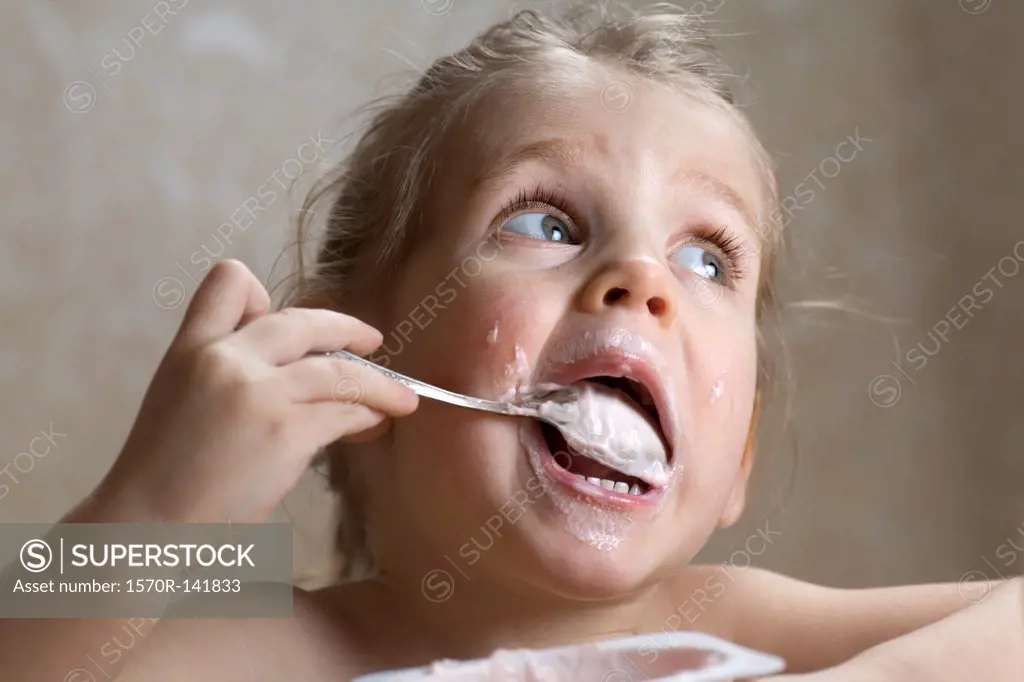 A young girl making a mess out of eating yogurt