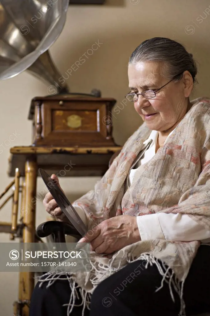 A senior woman looking intently at a vinyl record, gramophone in background