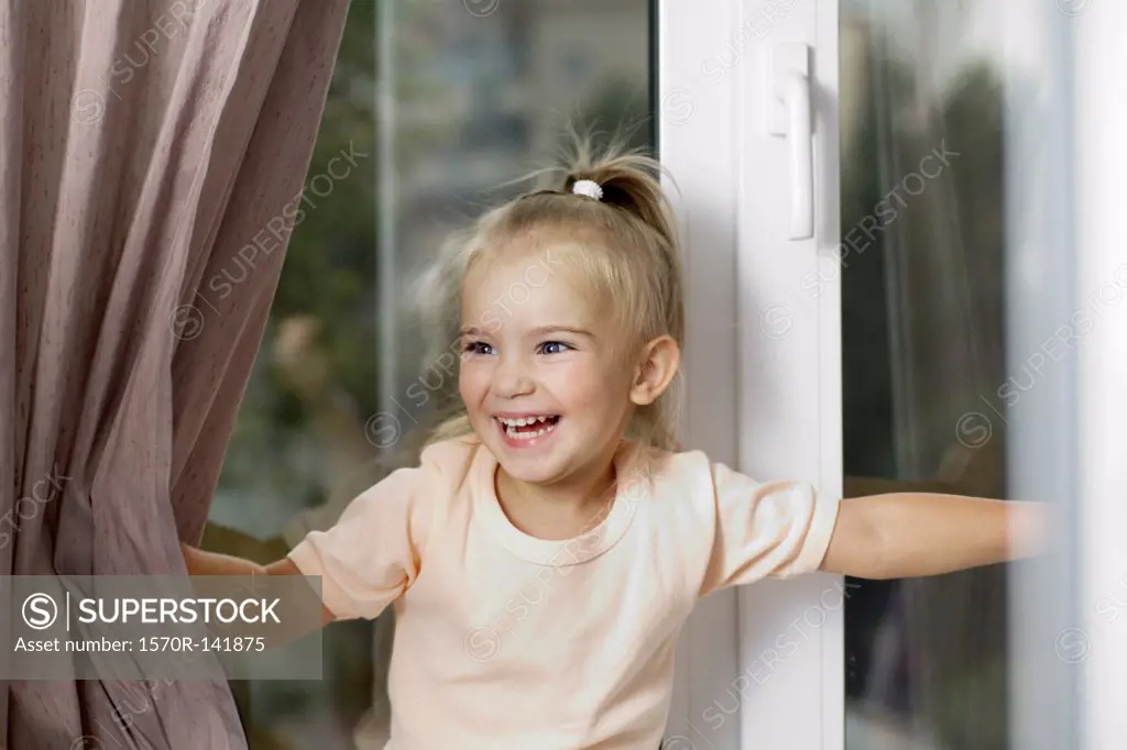 A young laughing girl pushing window curtains apart