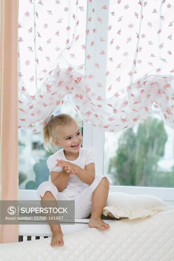 A young girl sitting on a window sill, clapping hands excitedly