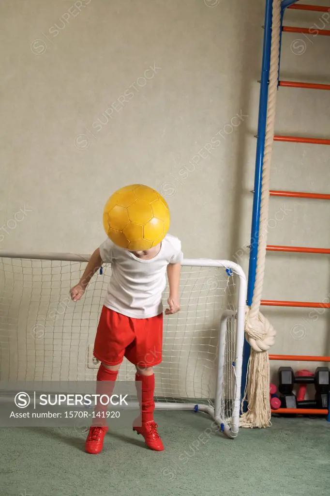 A young boy jumping to head butt a soccer ball away from a goal
