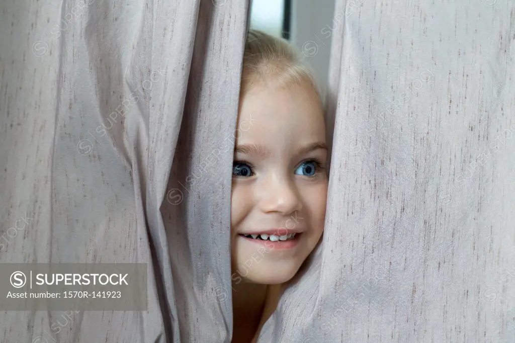 A young girl hiding between window curtains