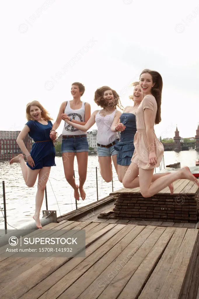 Five young female friends jumping in the air on a jetty next to the Spree, Berlin, Germany