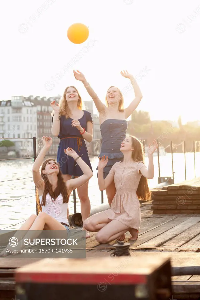 Four female friends tossing a ball around on a jetty next to Spree River, Berlin, Germany