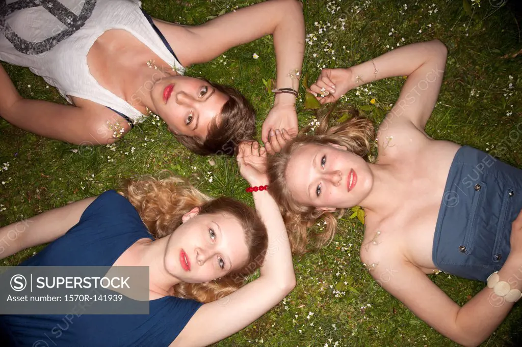 Three female friends lying in the grass in a circle looking sensually at the camera