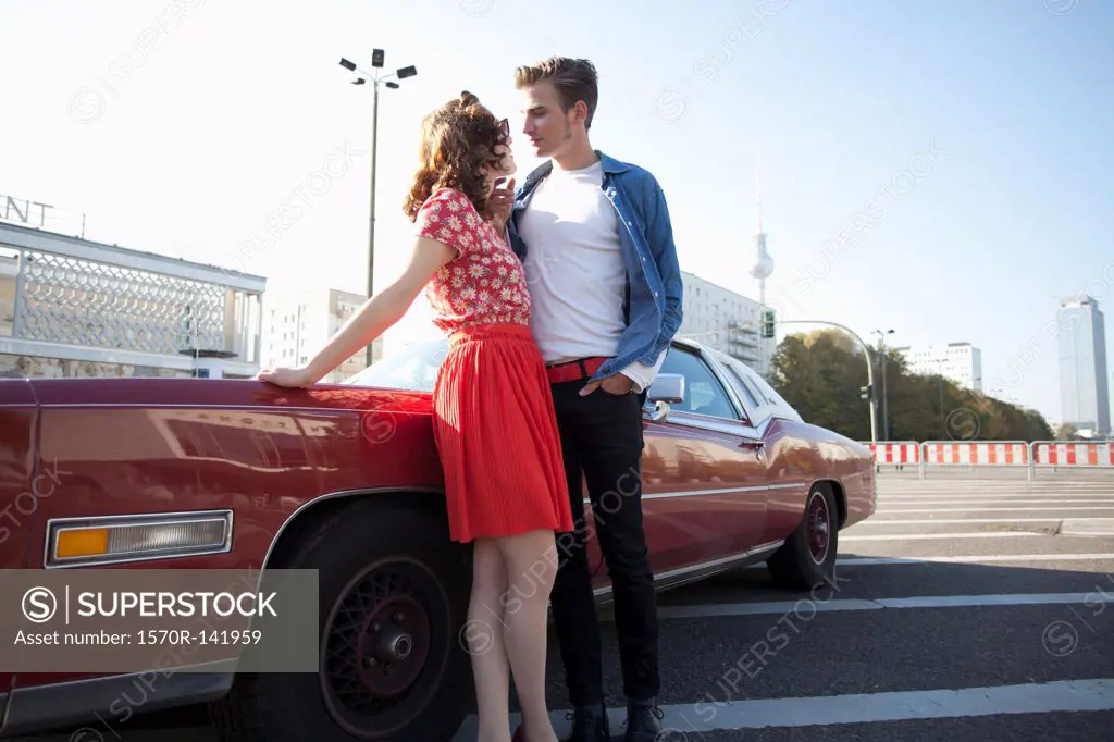 A flirtatious rockabilly couple standing next to a vintage car, Berlin, Germany