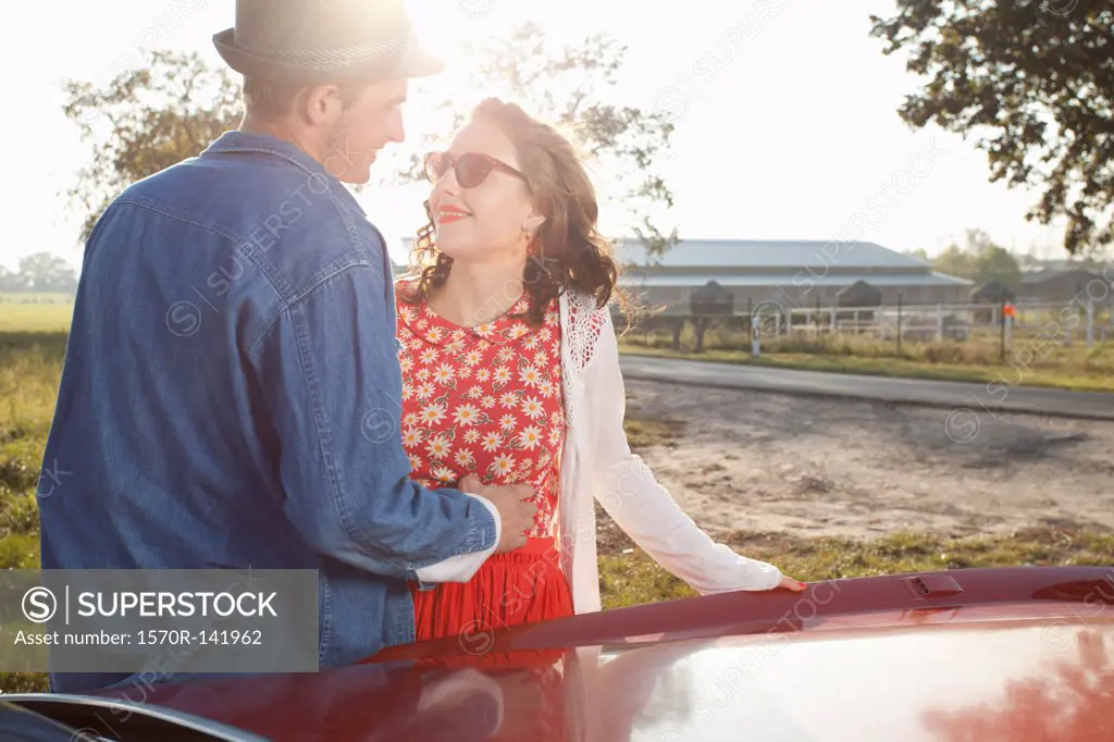 A flirtatious rockabilly couple standing next to a vintage car