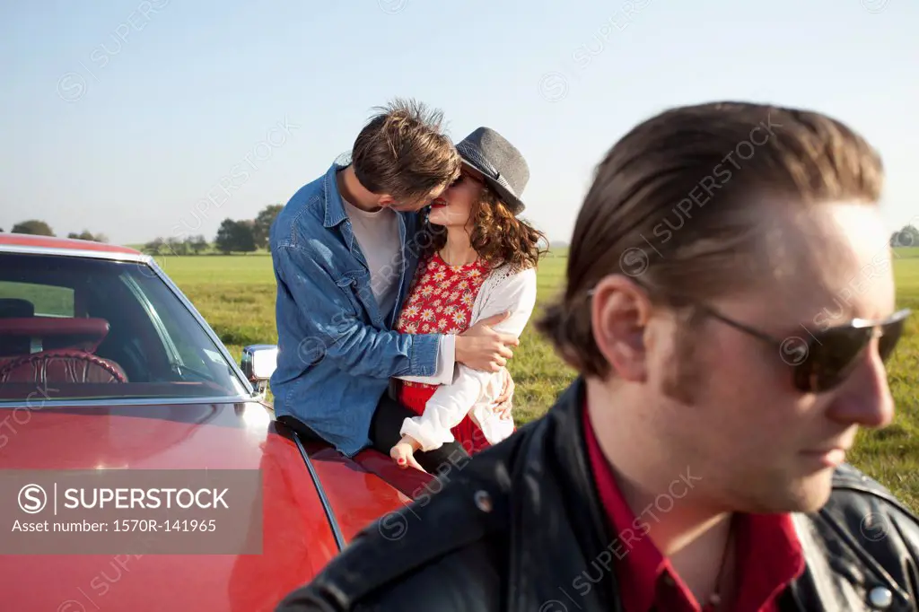 A rockabilly couple kissing while leaning on a vintage car, man in foreground