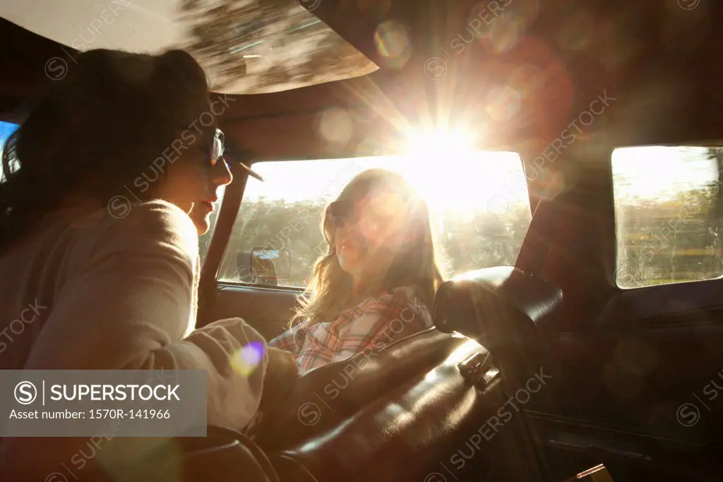 Two serene rockabilly women in the front seat of a vintage car