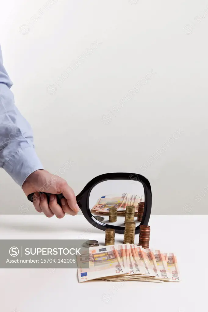 A man holding a hand mirror up to a pile of European Union currency
