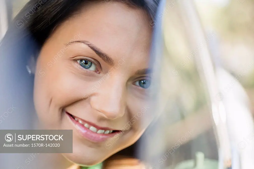 A beautiful young woman smiling while peeking through a car window
