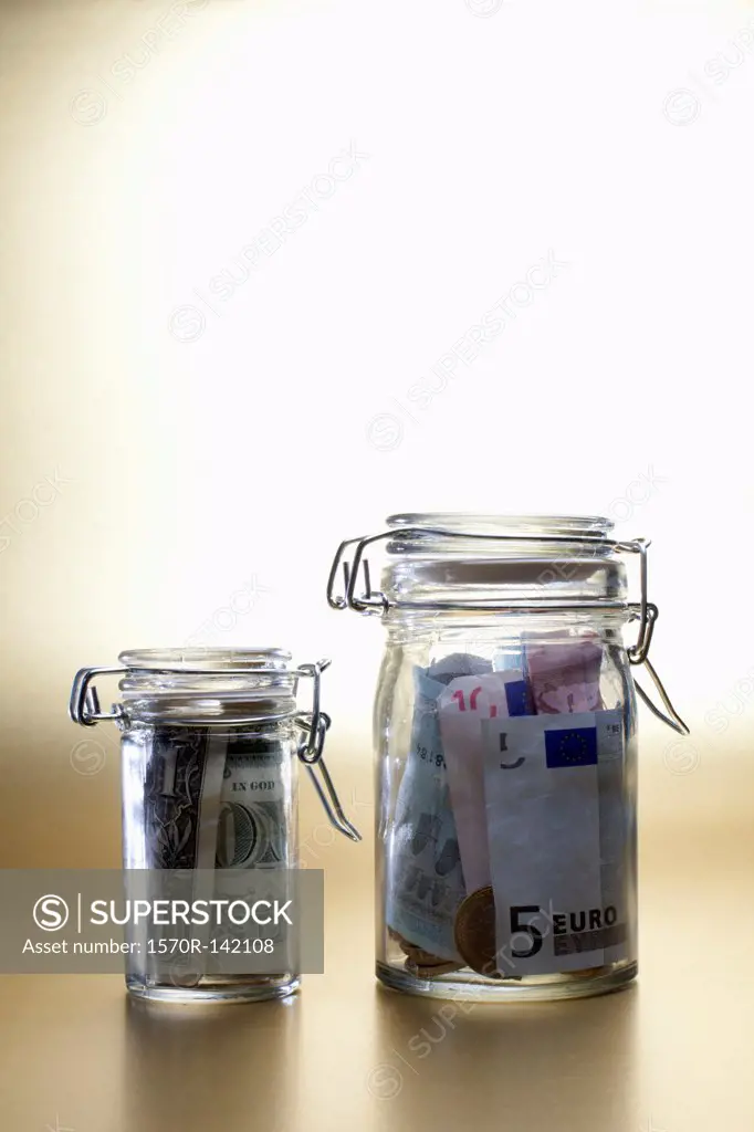 Dollar in a little jar beside larger jar full of euros