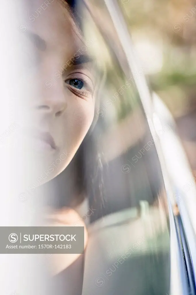 A young woman in a stationary car looking serenely out the window