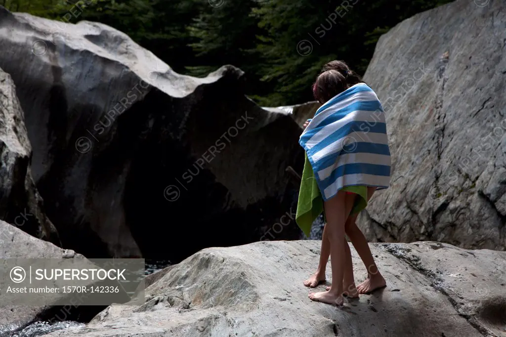 Two children wrapped in towels and standing on rocks