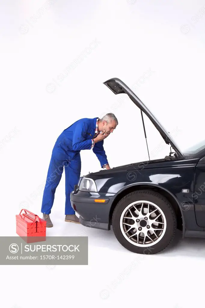 An auto mechanic looking under the hood of a car with uncertainty