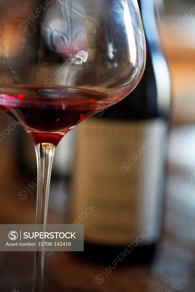 A wineglass with red wine in it and two bottles of wine in background