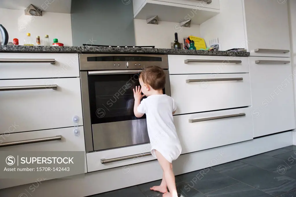 A toddler leaning on an oven door, peeking inside