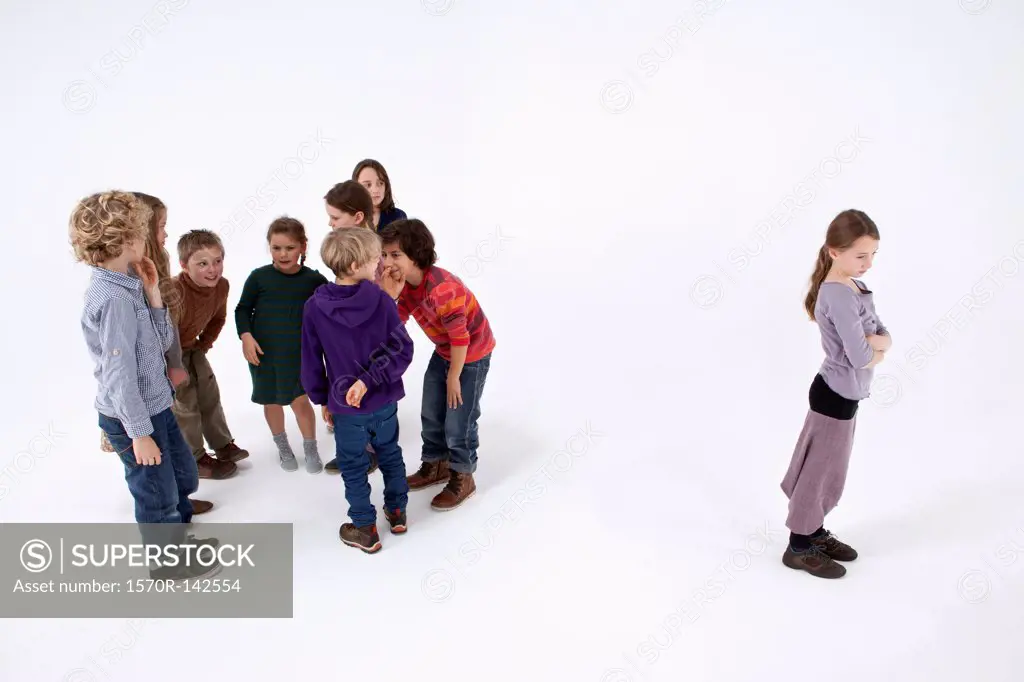A girl standing alone, arms crossed, while a group of kids gossip about her
