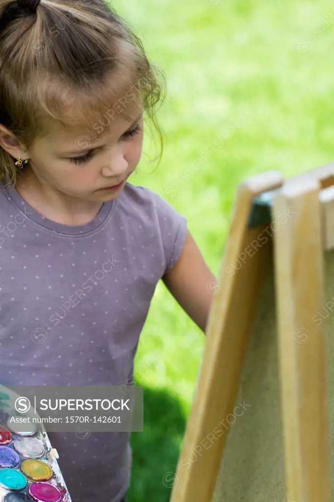 A young girl concentrating seriously while she's painting on an easel