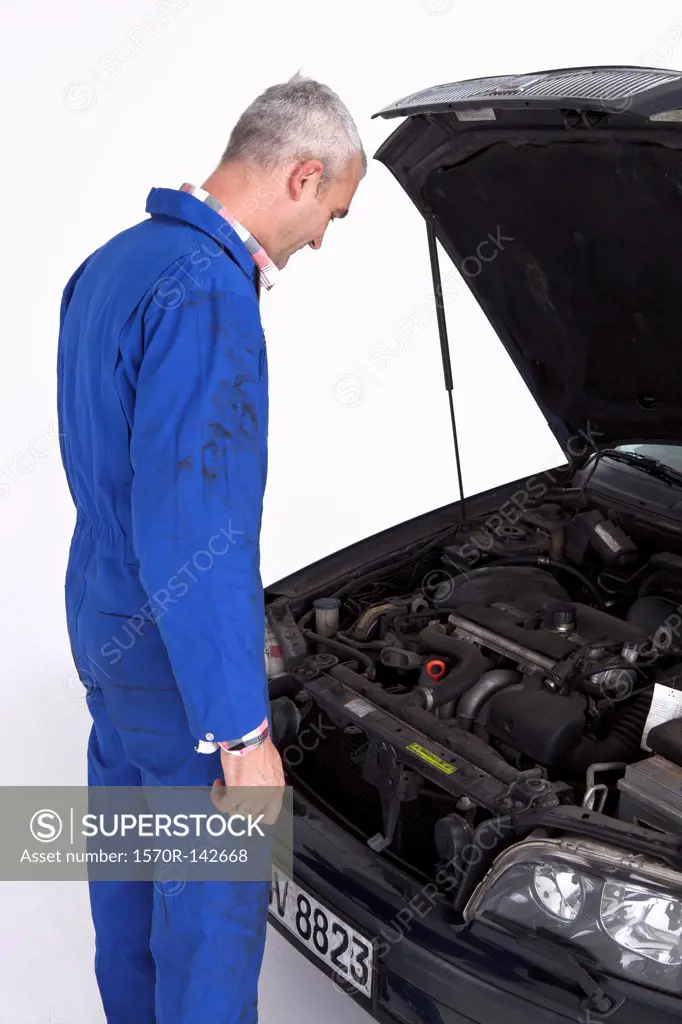An auto mechanic looking under the hood of a car thoughtfully