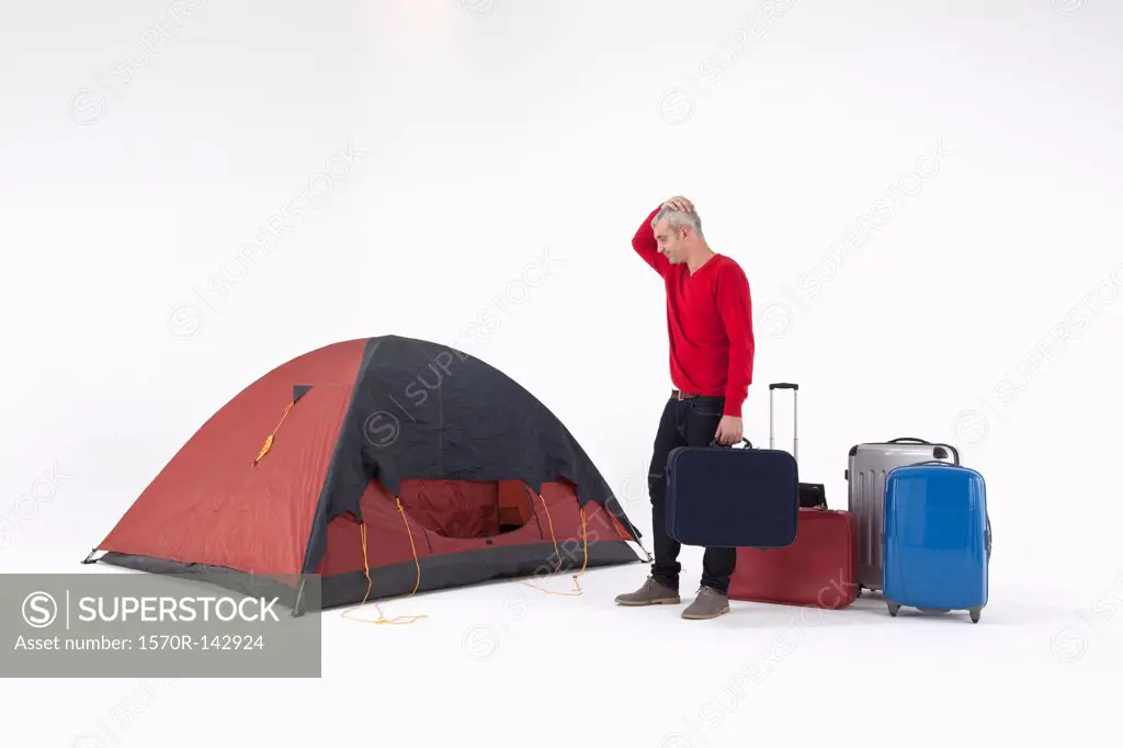 An unhappy man with loads of luggage looking at a tent with uncertainty