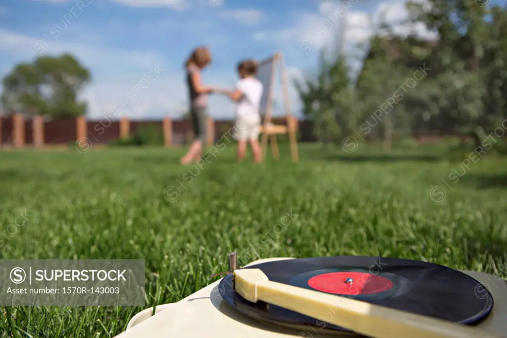 An old-fashioned record player on a lawn, children in background