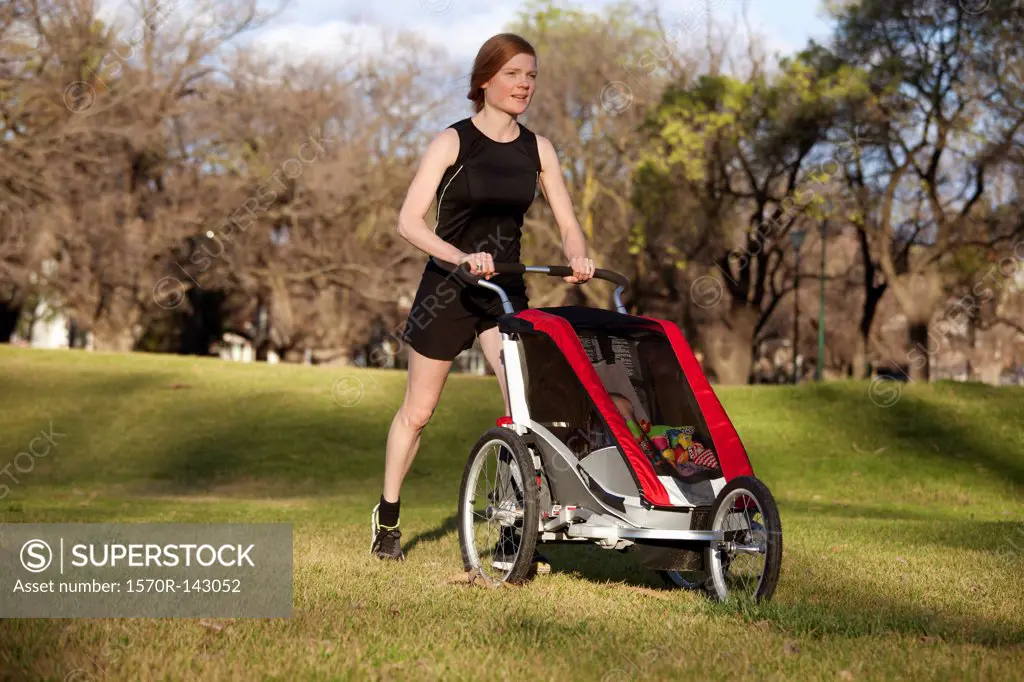 A woman jogging in a park and pushing a baby stroller