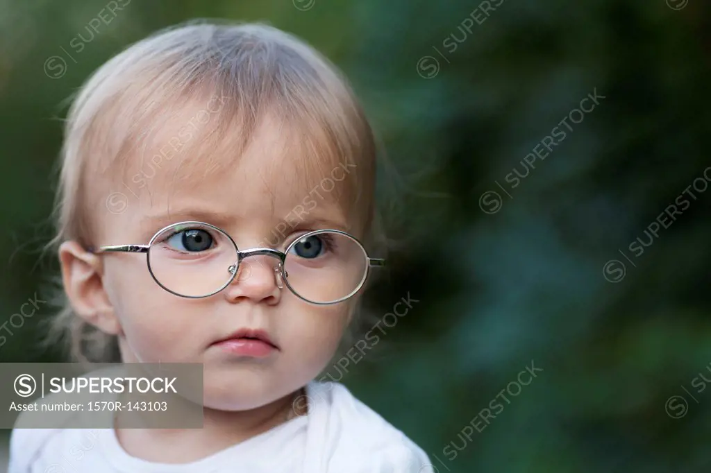 A young girl wearing glasses frowns in concentration while looking away