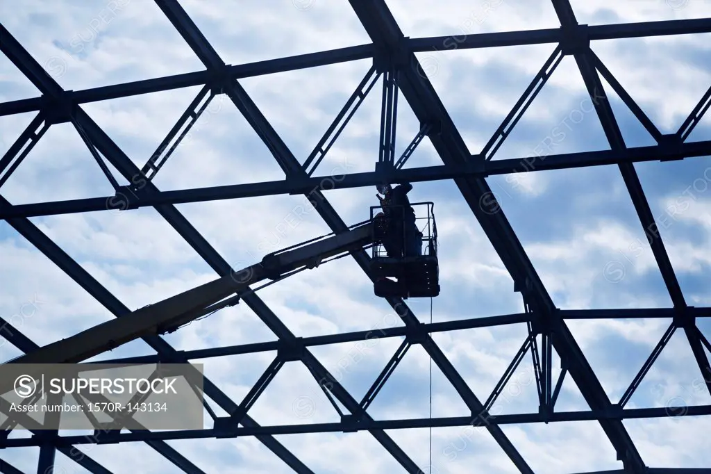 Welder on crane welding roof beam