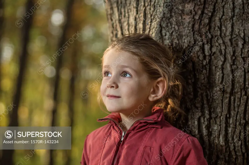 A young girl leaning against a tree trunk