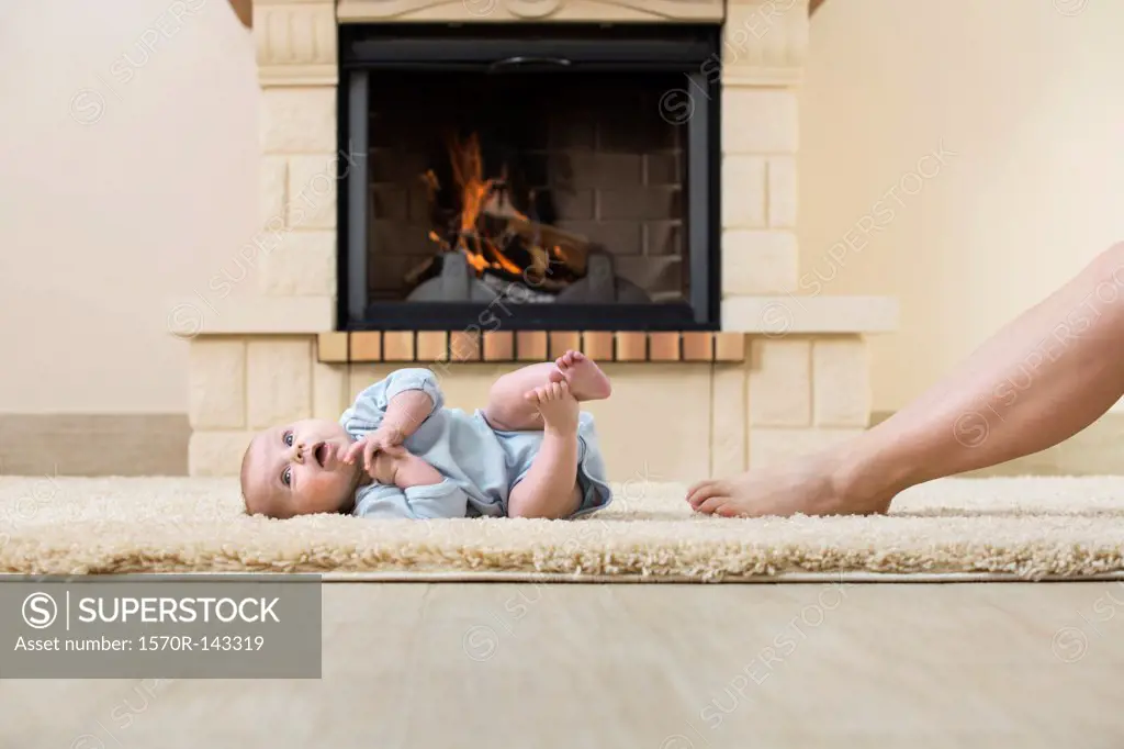 Baby and mother's leg on carpet in front of fire