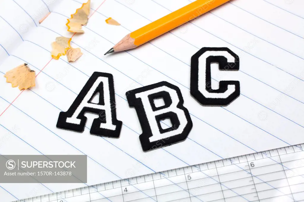 Varsity font stickers spelling out A, B, C atop a lined paper notebook with ruler and pencil
