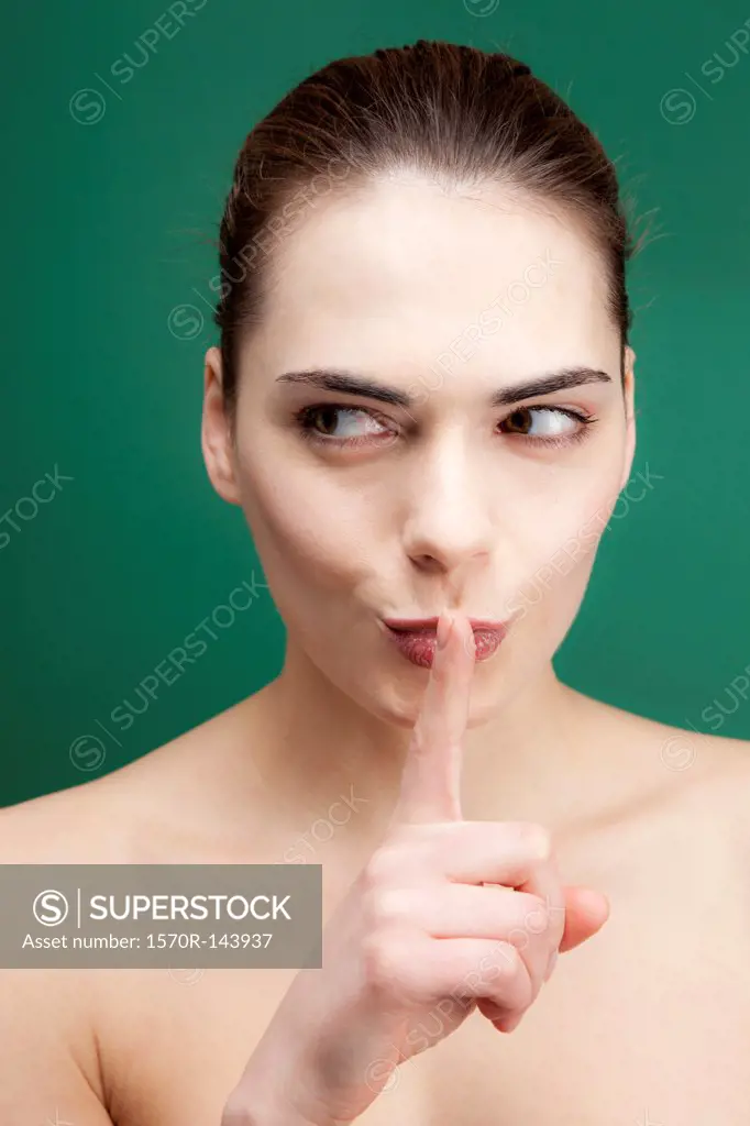 A young woman looking to the side while putting her finger to her lips playfully