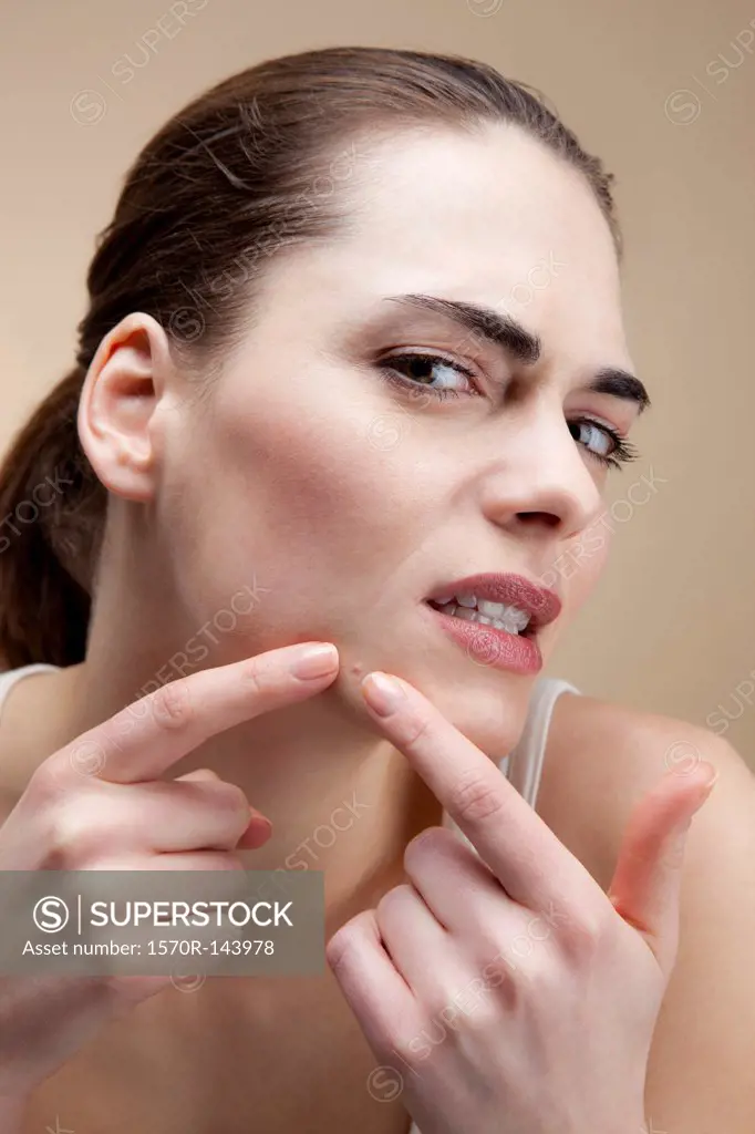 A young woman frowning in concentration as she squeezes a pimple