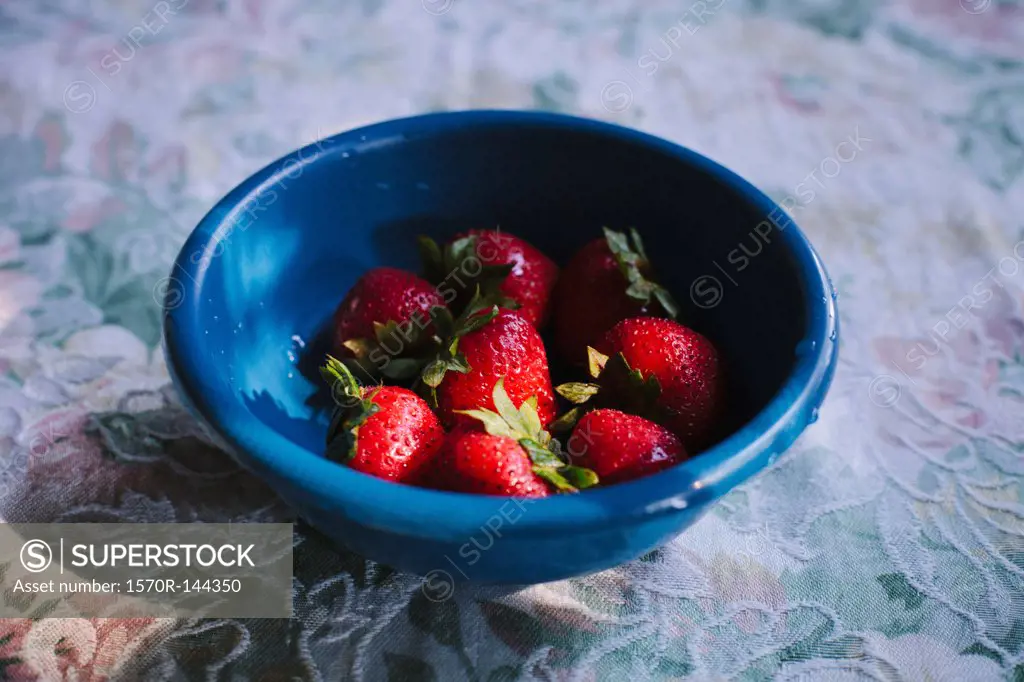 A bowel of fresh strawberries on a table with a patterned tablecloth