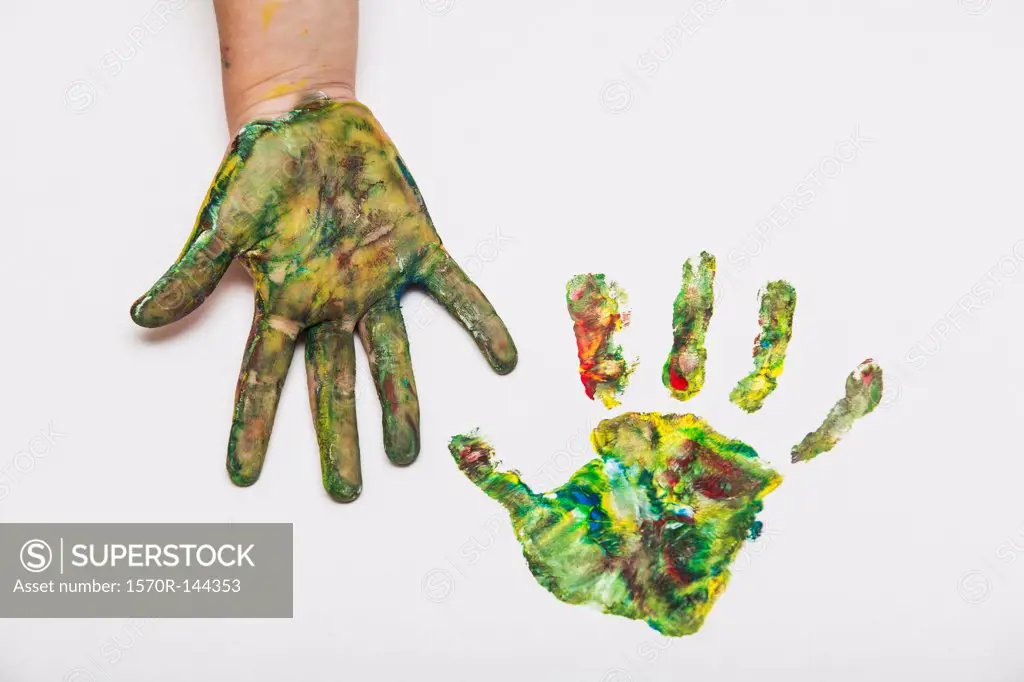 Child with colorful painted hand beside her hand print on paper