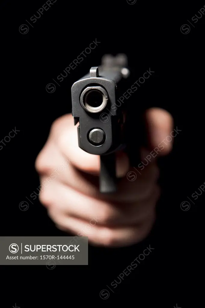 A hand holding a gun and pointing it at the camera, black background