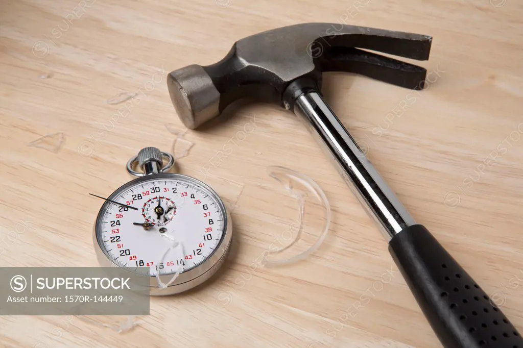 A claw hammer lying next to a broken stopwatch