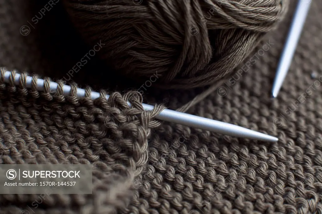 A pair of knitting needles, knitting and a ball of yarn, full frame