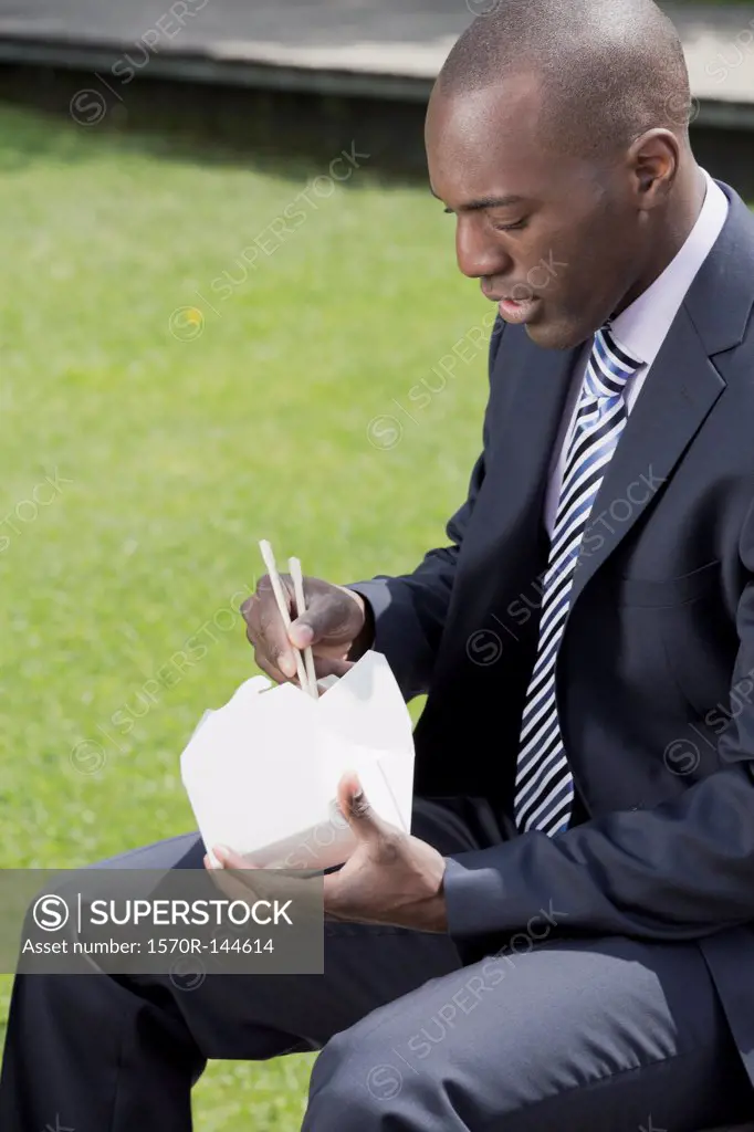 Businessman eating take away food with chop sticks outside