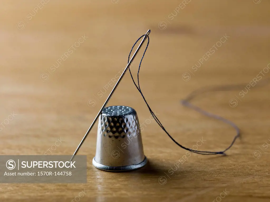 A threaded needle balanced against a shiny metal thimble