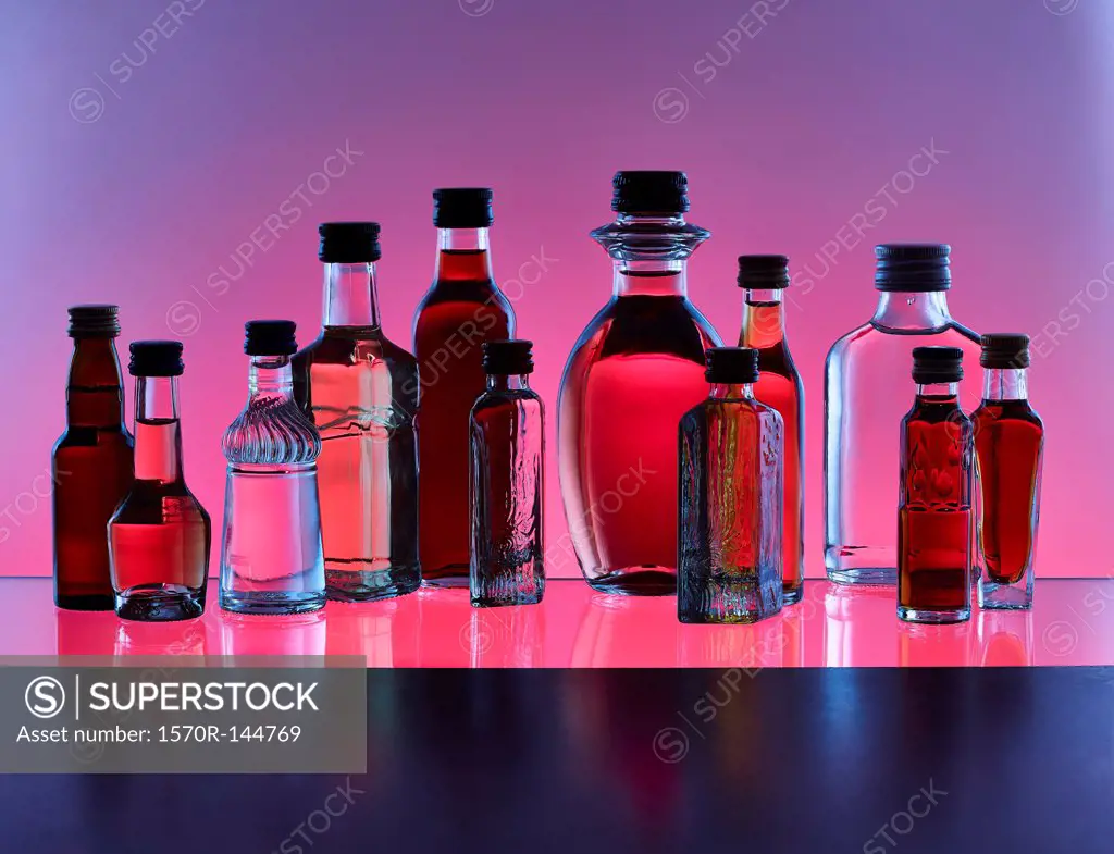 A grouping of various miniature bottles of alcohol without labels, back lit, colored background